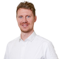 A white man with short reddish hair, wearing a white shirt, looking at the camera and smiling