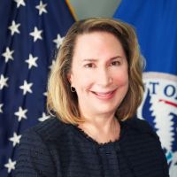A white woman with shoulder length light brown hair wearing a dark color jacket looking at the camera and smiling