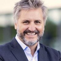 A white man with short spikey graying hair and facial hair, wearing a blue suit, smiling and looking at the camera